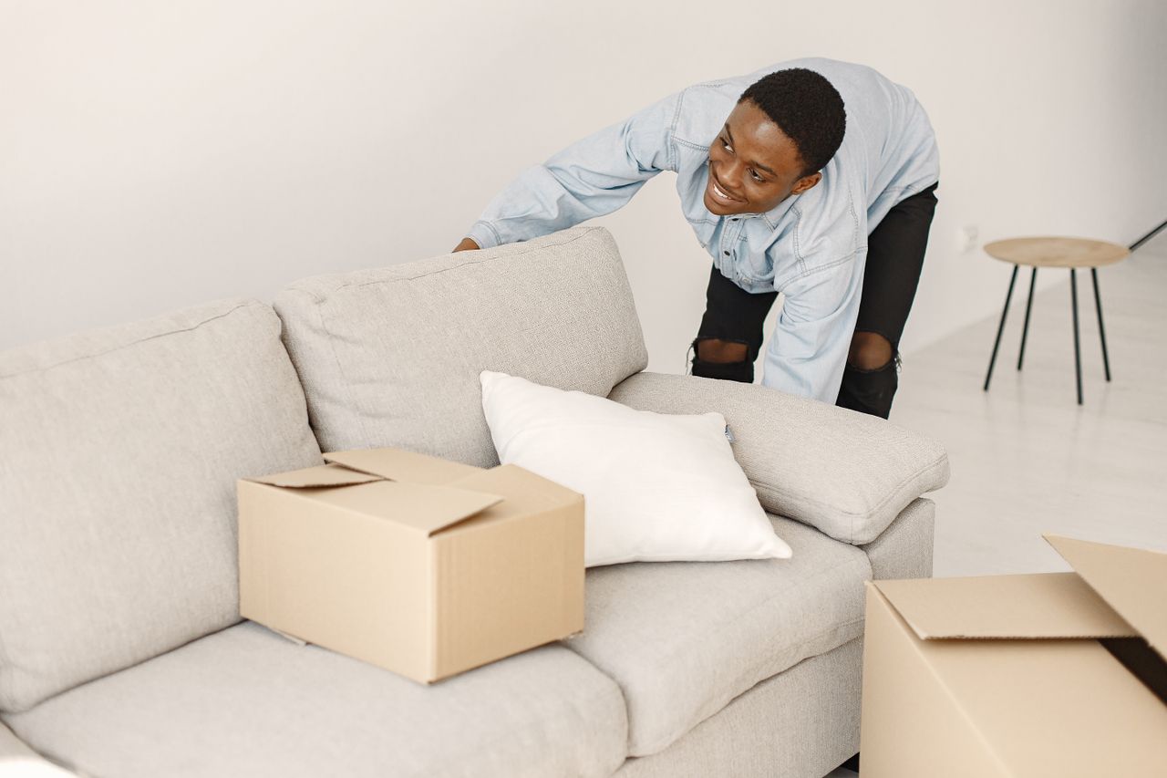 Jeune homme souriant en rangeant des cartons dans un salon moderne.
